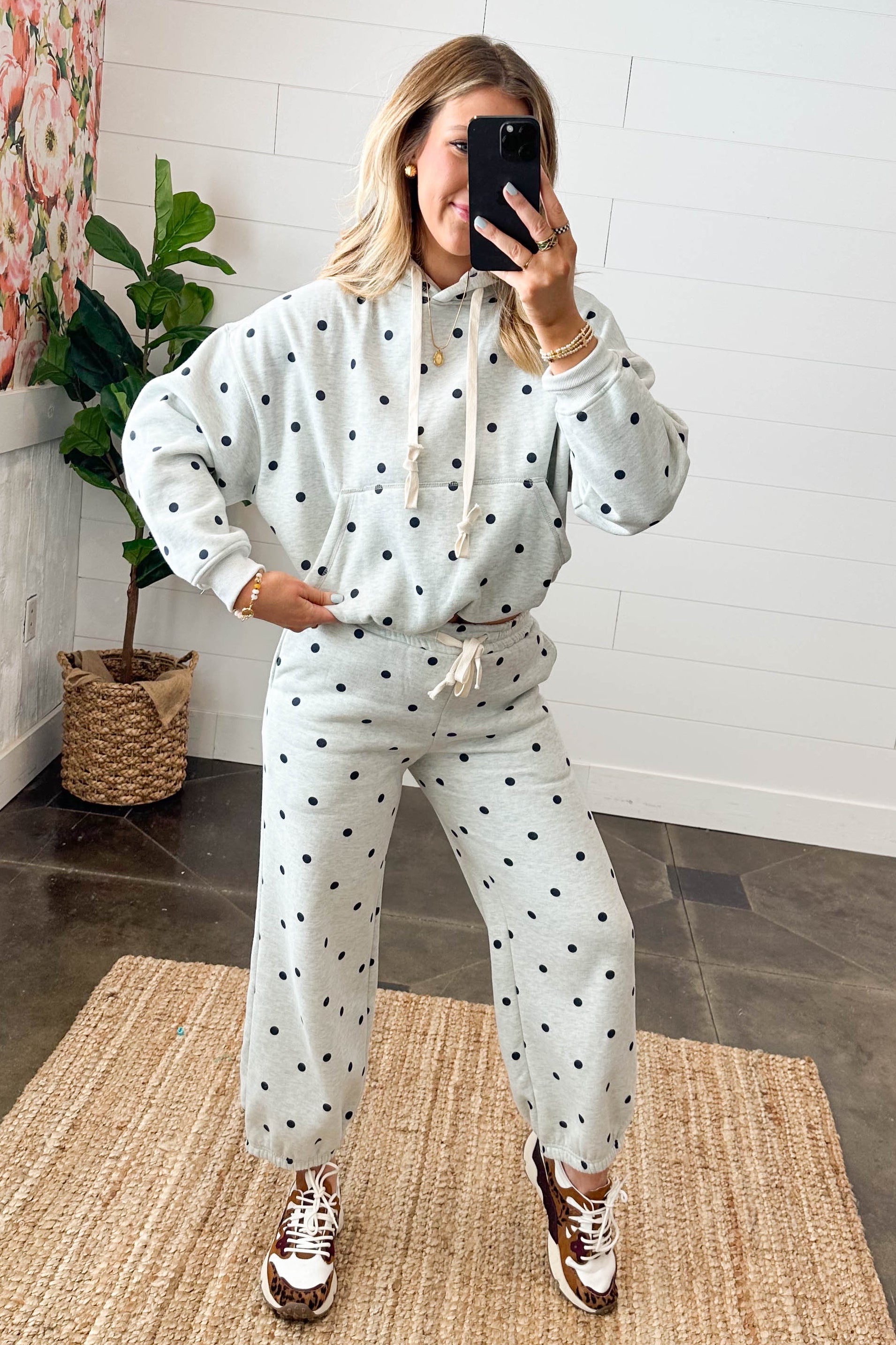 Person wearing a polka dot outfit taking a mirror selfie in a room with a floral painting and plant.